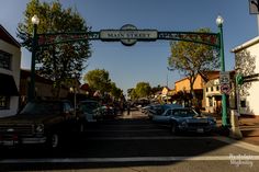 cars are parked in front of the main street entrance to an old fashioned shopping district