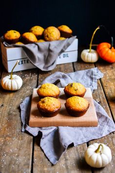 some muffins are sitting on a cutting board next to small pumpkins and gourds