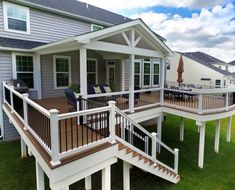 a deck with chairs and umbrellas in front of a large house on the grass