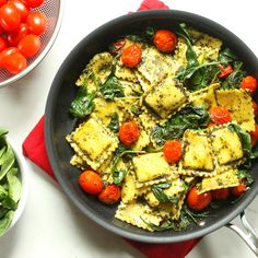 a skillet filled with pasta and vegetables next to a bowl of spinach leaves