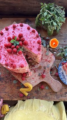 a cake with raspberries on it sitting on a cutting board next to other food