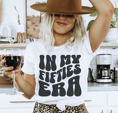 a woman holding a wine glass in her right hand and wearing a t - shirt that says on my fetties era