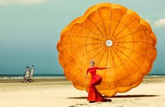 a woman in a red dress is holding an orange object on the beach with other people in the background