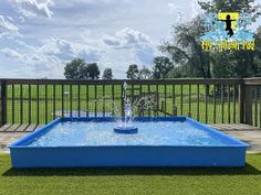 a blue pool with water spouting from it in the middle of some grass