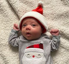 a baby is wearing a santa hat and laying on a blanket with his hands up