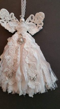 an angel ornament hanging on a black surface with white lace and pearls around it