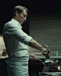 a man cooking food on top of a frying pan in a kitchen next to a stove