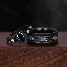 two wedding bands with black diamonds on them sitting on top of a wooden table next to each other