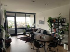 a living room filled with furniture next to a window covered in lots of books and plants