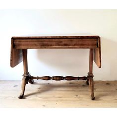 an old wooden table sitting on top of a hard wood floor next to a white wall