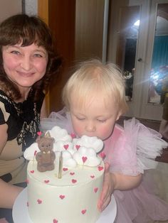 a woman holding a baby in front of a cake with white frosting on it