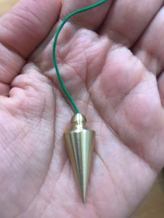 a hand holding a small metal object in it's left palm with a green cord