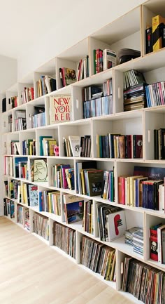 a book shelf filled with lots of books on top of a hard wood floor next to a white wall