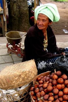 an old woman sitting on the ground next to baskets filled with nuts and other fruit