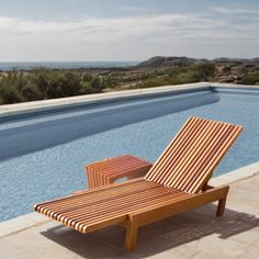 a wooden lounge chair sitting next to a swimming pool