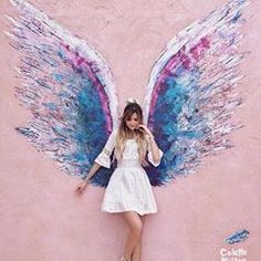 a beautiful young woman standing next to a wall with an angel wings painted on it