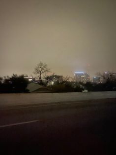 the city lights shine brightly in the distance as seen from an empty parking lot on a foggy night