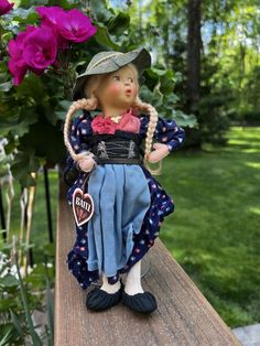 a doll sitting on top of a wooden table in front of purple flowers and greenery