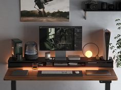 a desk with a monitor, keyboard and other items on it in front of a painting