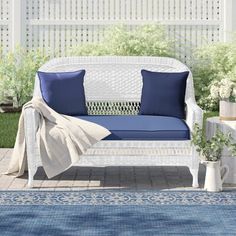 a white wicker couch with blue pillows on it in front of a pergolated area