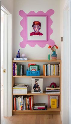 a bookshelf filled with lots of books in front of a painting on the wall