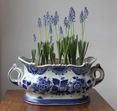 a blue and white vase filled with flowers on top of a wooden table next to a wall