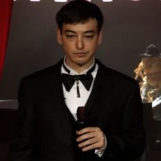 a man in a tuxedo standing next to a red curtain holding a bottle