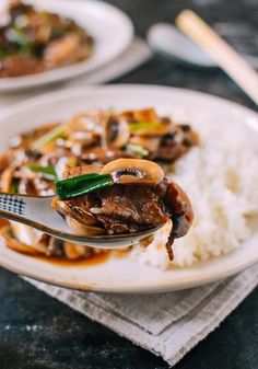 a spoonful of food on a plate with rice and mushrooms in sauce over it