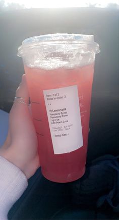 a plastic cup filled with pink liquid sitting on top of a car seat next to a person's hand