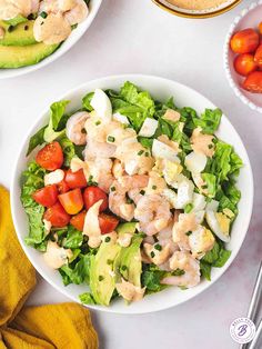 two white bowls filled with salad next to sliced tomatoes and avocado