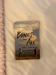 the book bones and all is laying on top of a white bed sheet with two people