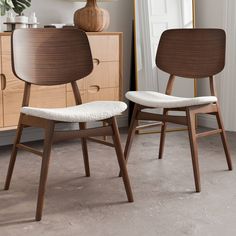 two wooden chairs sitting next to each other in front of a dresser and lamp on top of a table