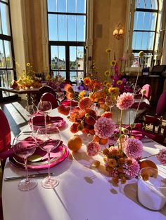 the table is set with pink and orange flowers in vases, plates and wine glasses