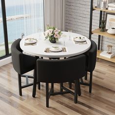 a dining room table with white chairs and plates on it, next to a window overlooking the ocean