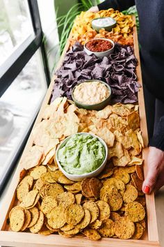 a wooden tray filled with chips and dips