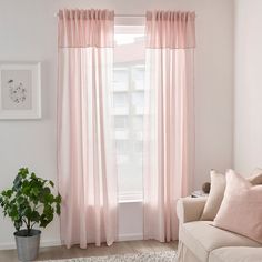 a living room with a couch, chair and window covered in pink drapes next to a potted plant