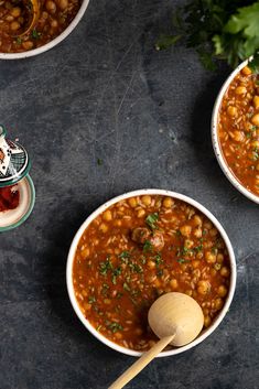 three bowls filled with beans and garbanzo on top of a black surface next to a wooden spoon