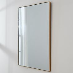 a mirror mounted to the side of a white wall next to a window in a room