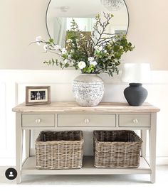 a white table with two baskets on it and a mirror over the top that has flowers in it