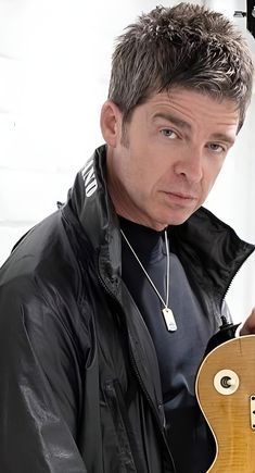 a man holding an electric guitar in his right hand and looking at the camera while wearing a black jacket