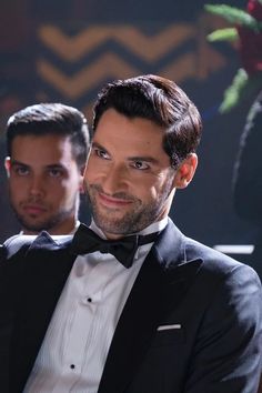 a man in a tuxedo smiles at the camera while another man looks on