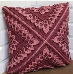 a red crocheted pillow sitting on top of a wooden table next to a brick wall