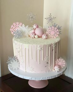 a pink and white cake with snowflakes on it sitting on a wooden table