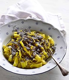 a white bowl filled with pasta covered in powdered sugar on top of a wooden table