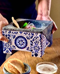 a person holding a blue and white bowl with food in it on top of a wooden table