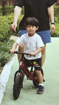 a young boy riding on the back of a red bike next to an adult's hand