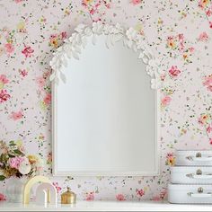 a white dresser topped with a mirror next to a wall covered in pink and yellow flowers