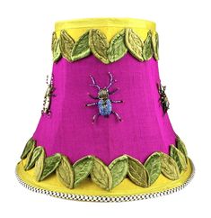 a pink lamp shade with green leaves and a lady bug on the bottom, sitting in front of a white background