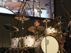 a man is playing drums on stage in front of a large screen with his hands behind him