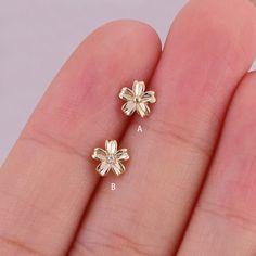 two small gold flowers are shown in the palm of someone's hand, one has a diamond on it